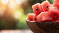 Fresh watermelon slices in wooden bowl with natural sunlight creating warm bokeh background for summer refreshment and healthy eating concepts.