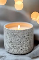 Lit aromatic candle in speckled ceramic holder with soft bokeh lights background creates cozy atmosphere for spa, meditation, or home decor styling.