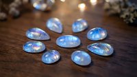 Luminous rainbow moonstone gems arranged in circle on wooden surface with warm bokeh lights creating magical atmosphere for jewelry design.