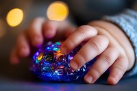 Small child's hand touching colorful illuminated sensory bubble pop fidget toy with glowing bokeh lights in background, creating calming therapeutic atmosphere.