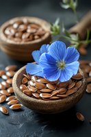 Fresh flax seeds in wooden bowls with bright blue flax flower on dark background, natural organic superfood and herbal medicine concept.