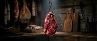 Aged raw meat hanging from chain in rustic butcher shop with cured products and wooden cutting boards, suitable for food industry, restaurant, and culinary content.
