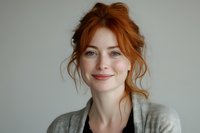 Young woman with red hair and gentle smile wearing casual grey cardigan against light background. Natural beauty portrait with soft lighting and minimal style.