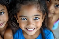 Cheerful young Asian girl with bright blue eyes and radiant smile wearing blue shirt, close-up portrait with soft bokeh background and natural lighting.