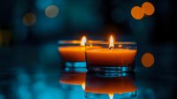 Two burning orange scented candles in glass holders with bokeh lights in dark blue background, creating cozy atmosphere for relaxation or meditation.