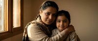 Loving Hispanic grandmother embracing young granddaughter in warm sunlit home interior showing family bond and intergenerational connection.
