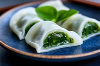 Fresh steamed dumplings filled with vibrant green spinach on blue ceramic plate, close up view showing translucent wrappers and leafy filling.