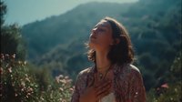 Young woman with eyes closed and hand on heart enjoying peaceful moment in mountain landscape with soft sunlight and wildflowers.