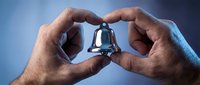 Male hands gently holding small silver bell in protective gesture against soft blue background for mindfulness meditation and spiritual practices.
