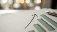 Business growth chart with upward arrow on desk with blurred office lights background for financial reports and presentations.