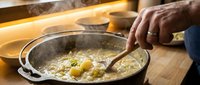 Professional chef cooking scrambled eggs in cast iron skillet on wooden cutting board in modern kitchen with warm lighting for culinary content.