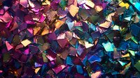 Vibrant metallic confetti pieces in pink, purple, gold and teal colors creating abstract mosaic pattern with shimmering light effect. Festive party background.