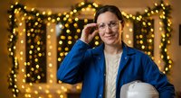 Professional Caucasian businesswoman in blue blazer adjusting glasses with warm bokeh lights background creating festive corporate atmosphere.