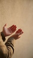 Open hands reaching upward in prayer or meditation gesture against warm textured wall background for spiritual wellness and mindfulness concepts.