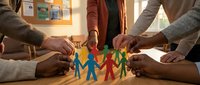 Diverse group of people joining hands around colorful paper cutout figures, symbolizing unity, teamwork, community support and collaborative partnership for charitable causes.