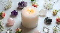 Burning white candle surrounded by healing crystals, gemstones and dried flowers on white background for meditation, wellness and spiritual practices.