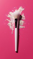 Makeup brush with scattered white loose powder creating splash effect on bright pink background. Professional cosmetic product photography for beauty industry.