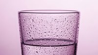 Purple textured glass with water droplets on pink background for beverage and drinkware photography concepts.