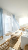 Bright, airy living room with white walls, natural wood furniture, and blue-white curtains framing glass doors. Neutral tones and minimalist Scandinavian design create a serene, light-filled space for home decor and interior design projects.