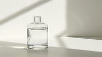 Clear glass bottle with pure water against white wall with natural window light and shadow creating minimalist composition for wellness and spa concepts.