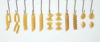 Assorted dried pasta shapes hanging from strings against white background, including fusilli, penne, farfalle and rigatoni for cooking and food styling.
