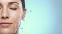 Young woman with closed eyes enjoying refreshing water splash on face for skincare and beauty routine on light blue background.