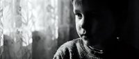 Young Caucasian boy in knitted sweater looking pensively out window in dramatic black and white portrait with natural lighting and emotional depth.