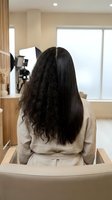 Woman with half straight half curly hair showing before after hair treatment results in modern salon chair for beauty transformation concept.
