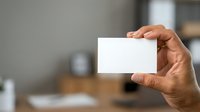 Man holding blank white business card in office environment for corporate branding and professional identity presentation.