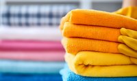 Stack of clean folded orange and blue towels with yellow rubber gloves, fresh laundry on blurred background. Housekeeping and cleaning service concept.