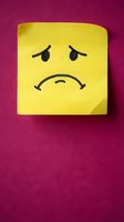 Yellow sticky note with sad face drawn in black ink on purple background expressing negative emotions and disappointment for office communication.