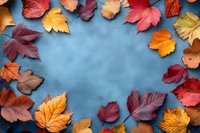 Colorful autumn leaves frame creating border on blue background with copy space in center, seasonal fall foliage arrangement in red, orange and yellow.