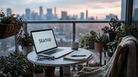Cozy balcony workspace with laptop displaying startup text, city skyline at dusk, plants, notebook, and coffee mug for remote work concepts.