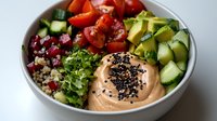 Fresh poke bowl with quinoa, cherry tomatoes, cucumber, avocado and creamy sauce topped with black sesame seeds in white ceramic bowl.