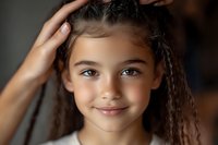 Young girl with long braided hair and warm brown eyes, mixed ethnicity, smiling at camera with hand touching head in casual pose for portrait and family photography.
