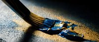 Artist paintbrush with vibrant blue acrylic paint on textured canvas surface. Creative art supplies for painting and artistic expression projects.