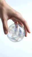 Hand protecting transparent glass sphere with swirling blue and white patterns inside, symbolizing care, protection and fragility on white background.