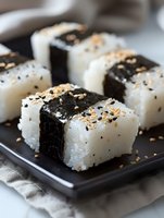 Fresh onigiri rice balls wrapped in crisp nori seaweed, topped with black sesame and roasted sesame seeds served on dark plate, close up view of Japanese cuisine.