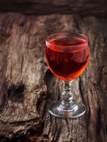 Glass of red wine on rustic wooden table with natural bark texture background for restaurant menu design and beverage advertising concepts.