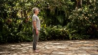 Senior Caucasian man in casual clothing standing peacefully on stone patio surrounded by lush tropical garden vegetation for wellness and retirement lifestyle.