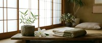 Zen spa setting with bamboo plant, white orchid flowers, folded towels on wooden table. Japanese-inspired wellness retreat interior with natural light.