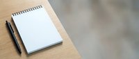 Open spiral notebook with blank white pages and black pen on wooden desk surface, suitable for writing, planning, and creative projects.