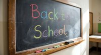Colorful chalk writing Back to School on classroom blackboard with wooden frame and chalk pieces on ledge for educational content and academic materials.