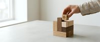 Hand placing wooden block with tree icon on stacked blocks, symbolizing growth, sustainability, and business strategy on a neutral background.