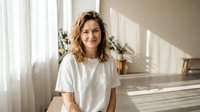 Happy young Caucasian woman with wavy blonde hair smiling in bright modern home interior with natural sunlight streaming through windows.