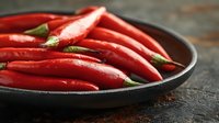 Fresh red chili peppers in cast iron pan on dark wooden background, close up view with selective focus and natural lighting for food photography.