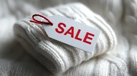 White knitted sweater with red SALE tag attached by string, showcasing winter clothing discount for seasonal retail promotion.