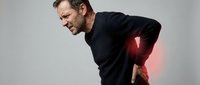 Middle-aged Caucasian man experiencing severe lower back pain with red highlight showing inflammation area on neutral background for medical concepts.