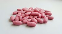 Pink oval tablets scattered on white surface for pharmaceutical medical healthcare supplement vitamin concept isolated background.