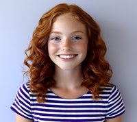 Young woman with natural red curly hair and freckles wearing striped navy and white top smiling warmly against light background.